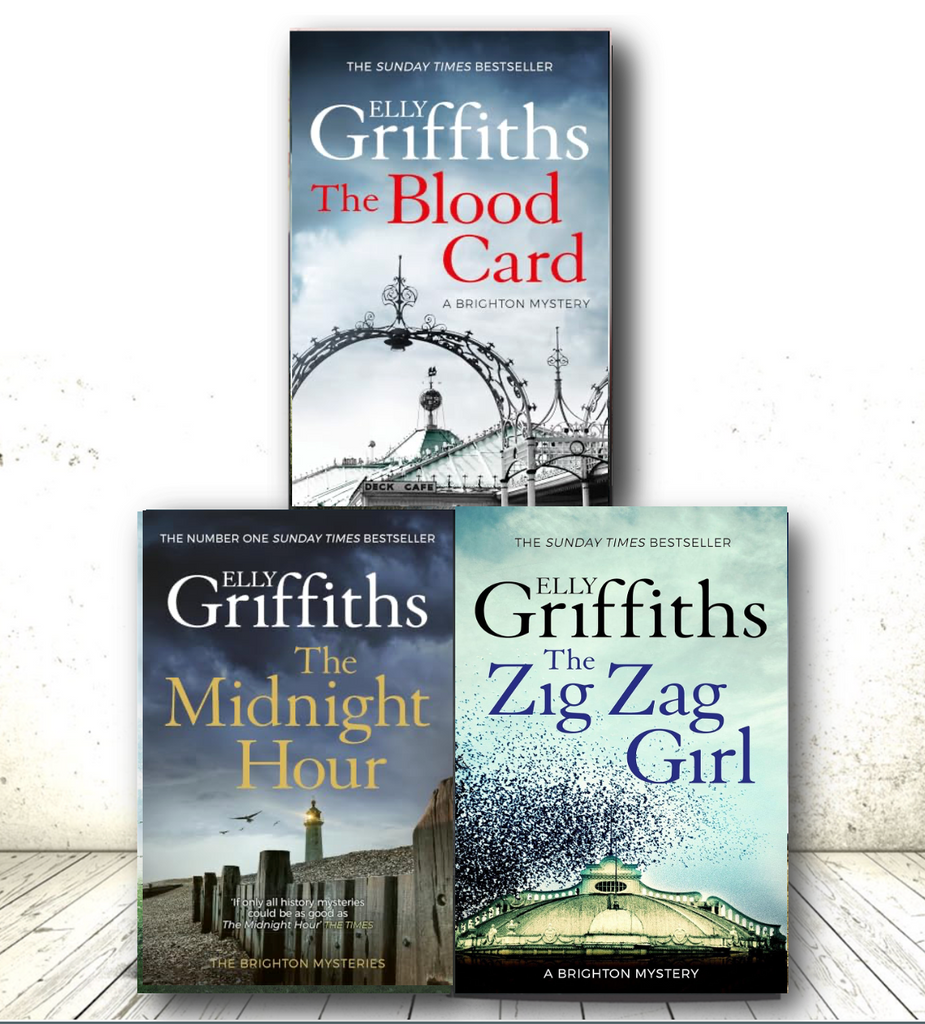 Three book covers by Elly Griffiths are arranged on a light wood floor against a white wall. The top cover reads 'The Blood Card' with a blue sky and arched bridge scene; the bottom left reads 'The Midnight Hour' with a lighthouse and gray bridge; the bottom right reads 'The Zig Zag Girl' with a bird-filled sky and bridge.